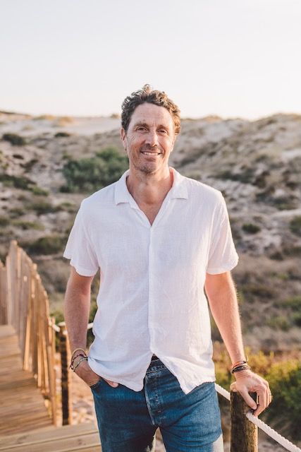 Jonathan Binder smiling on a wooden boardwalk through the dunes at golden hour