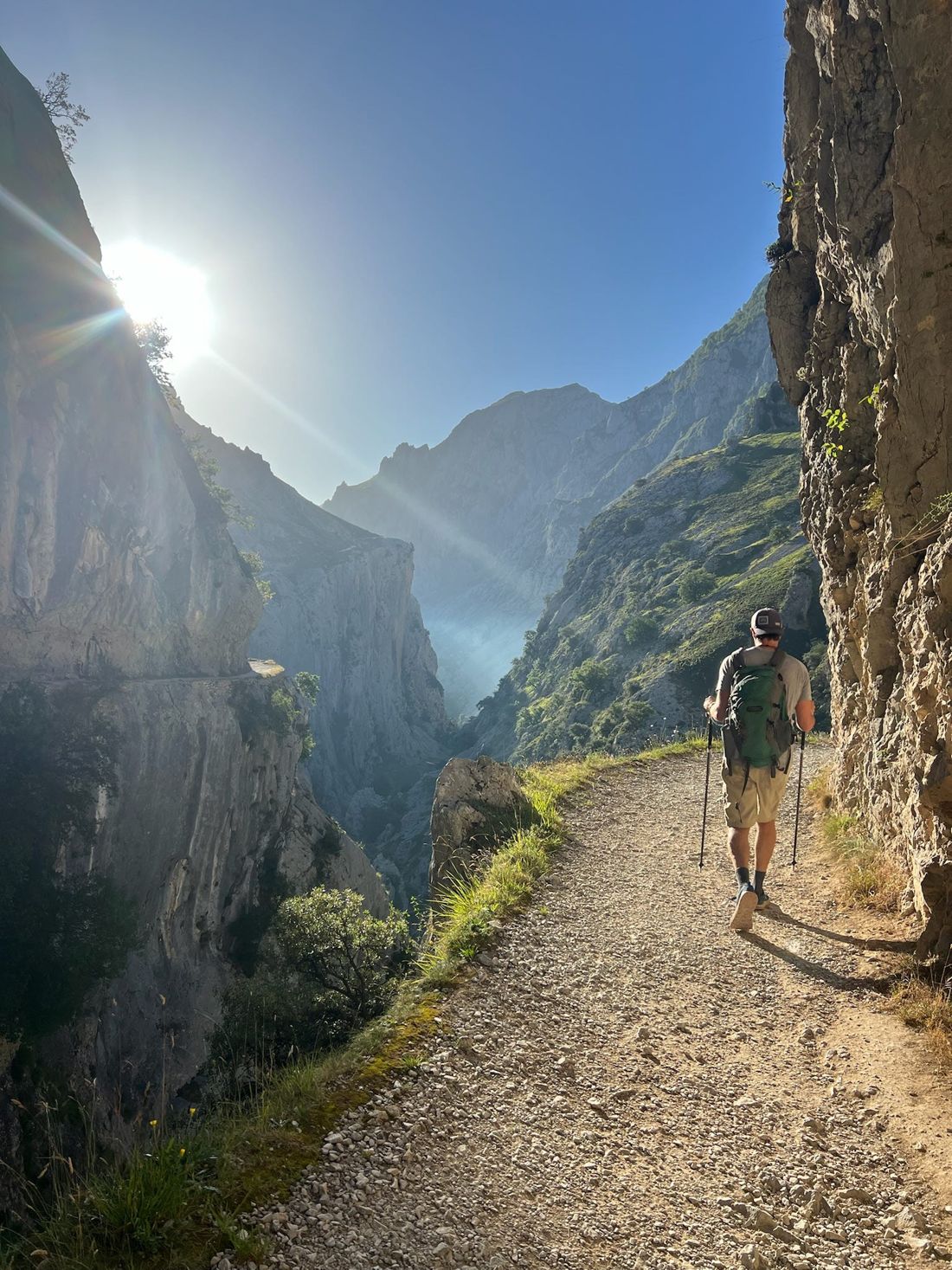 A hiker walking a narrow mountain path along a sunlit gorge